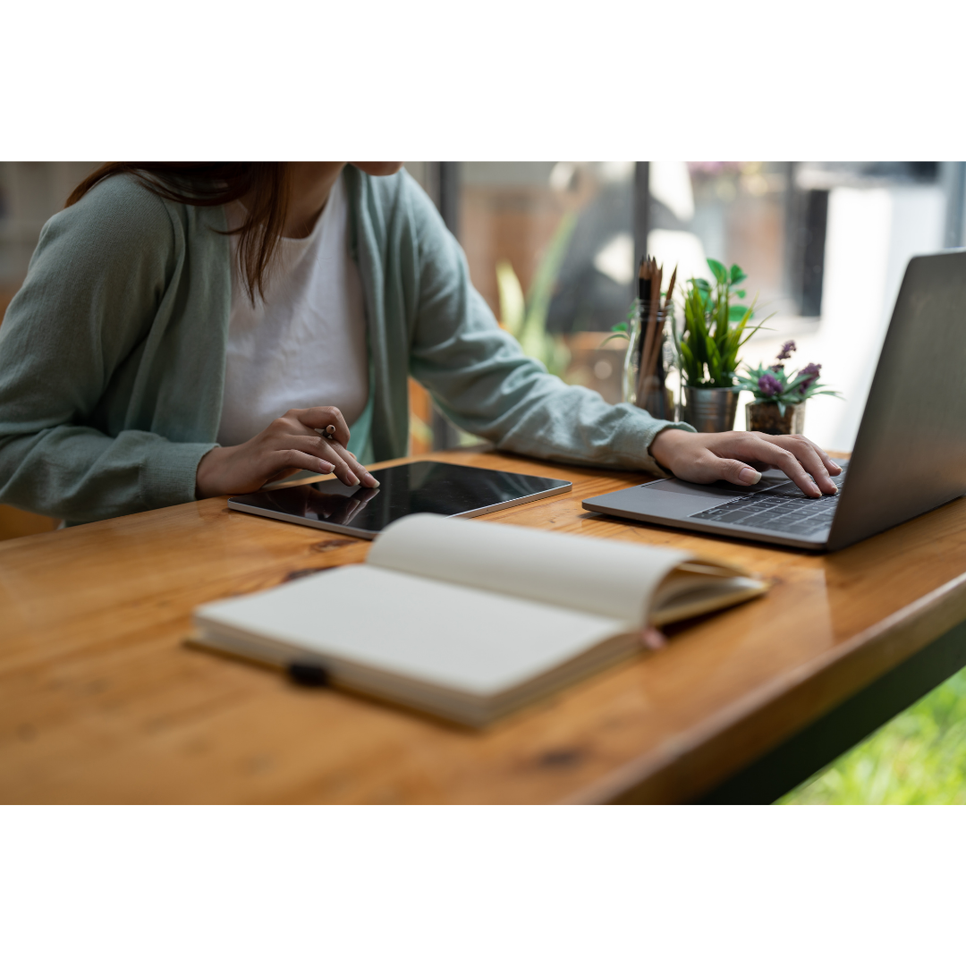Frau arbeitet am Laptop Eine Frau sitzt am Laptop und bearbeitet etwas. Ein offenes Notizbuch liegt vor ihr.